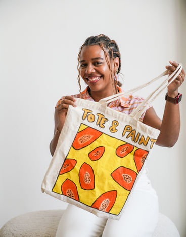 Yéléna, founder of Tote and Paint, holding a tote bag she painted with orange papayas