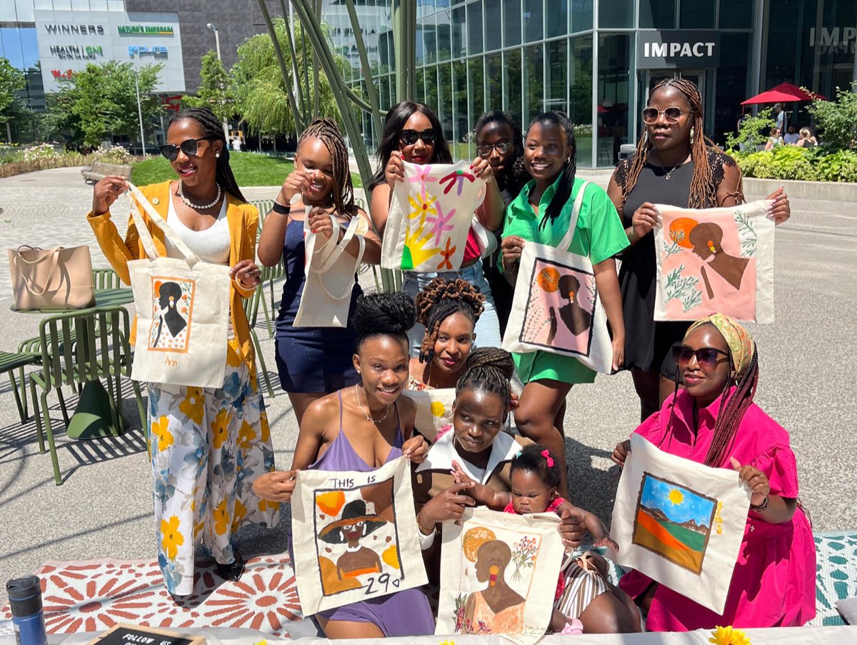 A group of friends outdoors in the city, each holding up the tote bag they painted